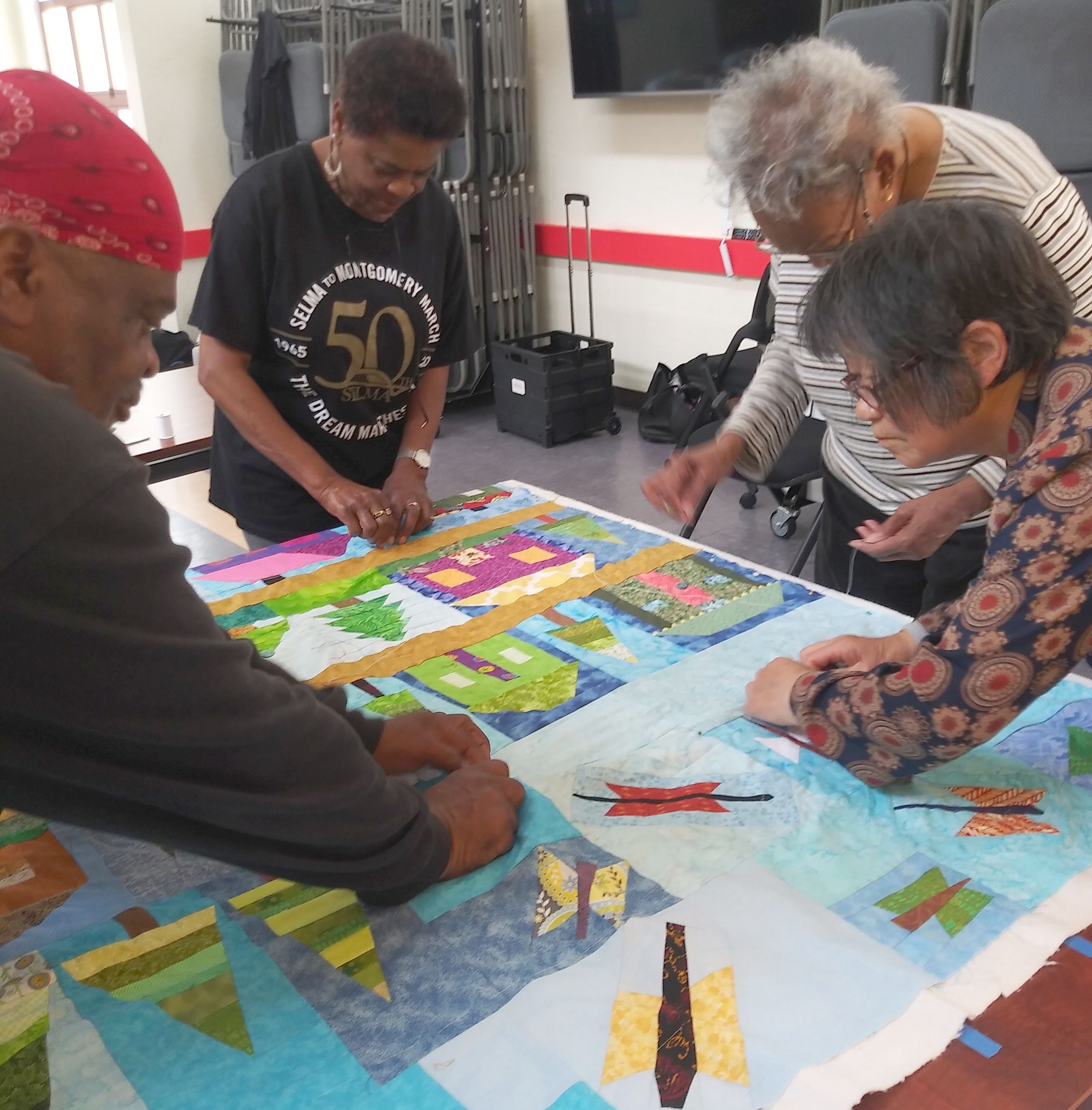 three quilters with a manycolored quilt.