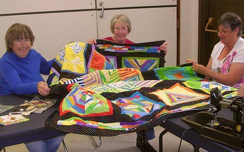 three quilters with a manycolored quilt.