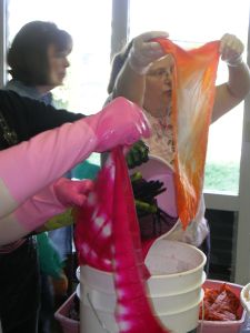 three women pull wet dyed cloth from bucket