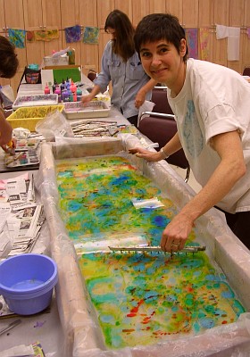 Woman in white T shirt combs drops of yellow red and green floating dye in a marbling tray.
