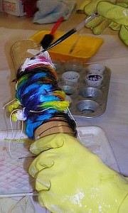 Hands in yellow gloves put dye on silk wrapped round a tube.