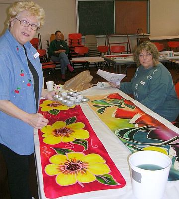 Two women painting silk scarves: yellow flowers on red